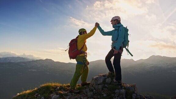 两个登山运动员在阳光下欣赏山顶的美景并握手