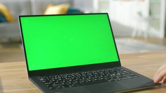 在舒适的客厅里一名男子坐在办公桌前使用绿色模拟屏幕的笔记本电脑