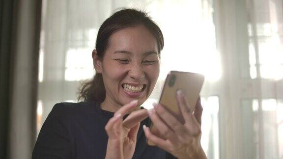 慢镜头亚洲女人在家里用智能手机庆祝我的成功