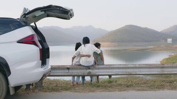 亚洲母亲和两个女儿坐在汽车后备箱后一起玩耍享受假期野餐在大坝公园与美丽的自然景观