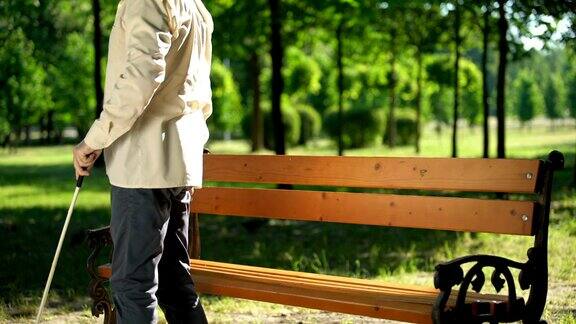 盲人拄着拐杖从长凳上站起来在夏季公园散步放松