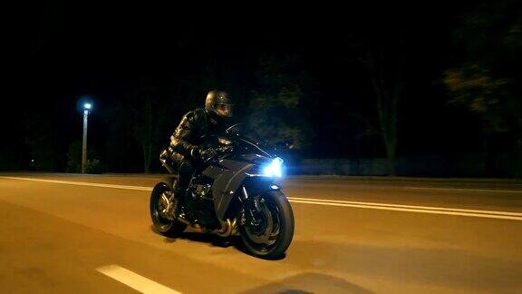 一个戴着头盔的年轻人骑着现代黑色摩托车在夜晚的城市街道上飞驰一个骑摩托车的人在空旷的夜里与他的摩托车赛跑人驾驶自行车自由和爱好近距离