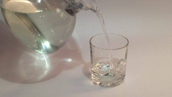 将纯净的水从壶中倒入白色背景的透明玻璃杯中健康饮食理念水注入透明的玻璃杯慢动作镜头