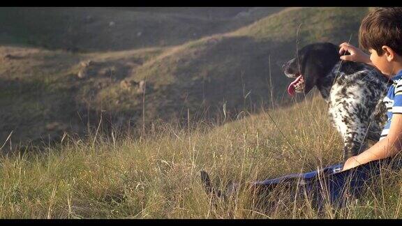 男孩和狗坐在山坡上看日落