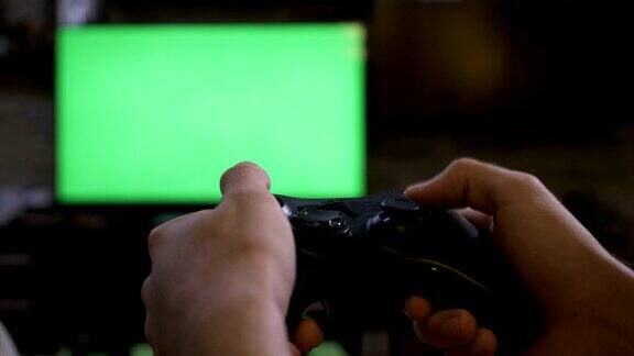 特写的年轻男性的手玩视频游戏控制台控制杆上的色度键绿色屏幕电视屏幕