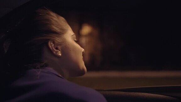 从车里看:美丽的年轻女子从车窗里探出身子看着夜晚的城市Slowmotion拍摄