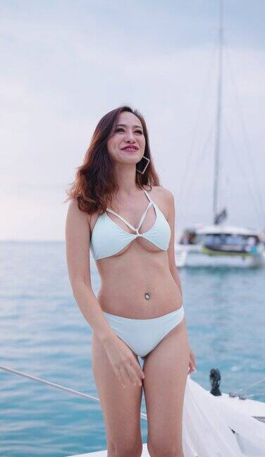 中年性感的亚洲女性在游艇上欣赏美丽的海景一位迷人的亚洲女子穿着白色两件套比基尼站在豪华游艇前享受日光浴她非常快乐和开朗享受暑假豪华的船
