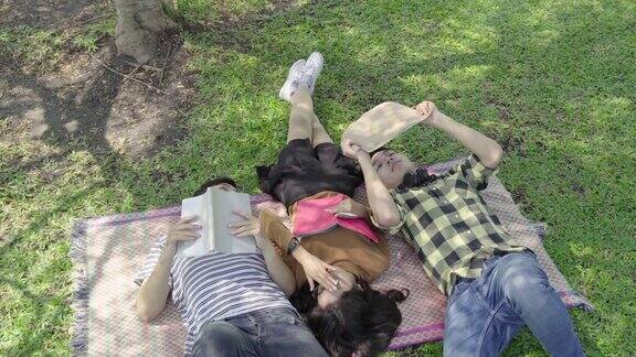 一群亚裔大学生坐在公园里看书