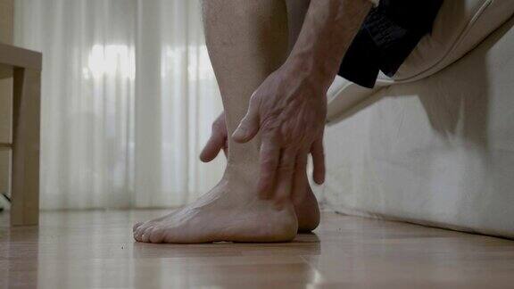 病人成熟的男人与关节炎坐在床上摩擦他的脚踝和脚缓解疼痛