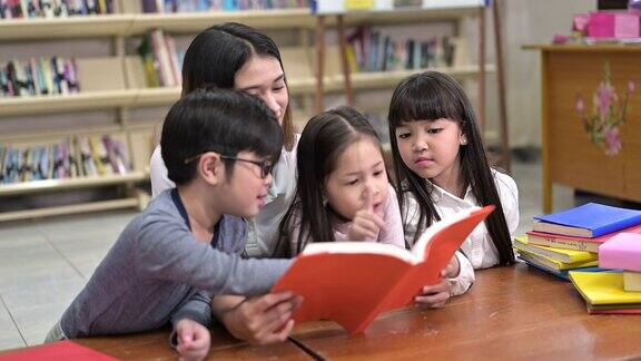 一群亚洲孩子在学校图书馆和老师一起读书背景是书架