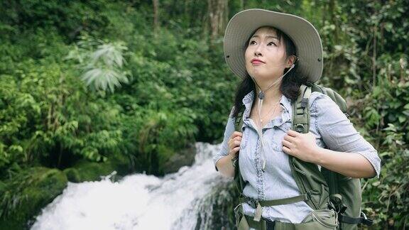 一位年轻女子站在山上的一条小溪边徒步旅行