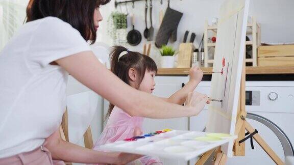亚洲年轻快乐的女儿和妈妈在画板上画画快乐的家庭活动小女孩学习如何用水彩画和画笔画画享受与妈妈的创造力