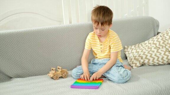 一个白人男孩坐在家里客厅的沙发上玩着一个抗压力的popit玩具
