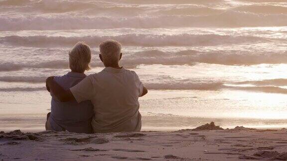 老夫妇在海滩上看太阳在海洋上落下的后视图