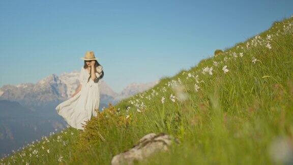 一位身穿白色长裙、头戴帽子的年轻女子走在长满水仙花的草地上