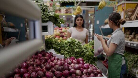 友善的女售货员用一个装着洋葱的塑料袋帮顾客挑选洋葱
