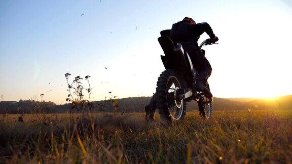 越野摩托车的轮子开始旋转踢起地面或泥土摩托车开始运动骑摩托车的人在日落时分骑车美丽的风景作为背景慢镜头