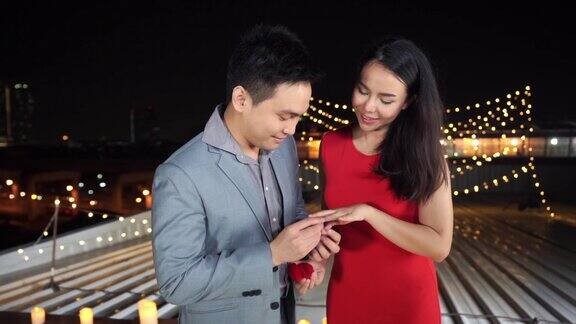在浪漫的夜晚快乐的亚洲情人男人通过给她美丽的结婚戒指和求婚来表达惊讶的穿着红色礼服的美丽女人浪漫的求婚概念