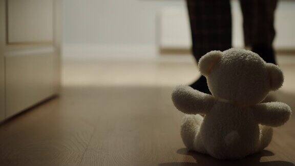 一个男人经过一个独自坐在地板上的小毛绒熊玩具