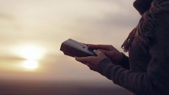 一个女孩在户外读《圣经》日落时分在山顶研究上帝的话语在圣经中寻找真理