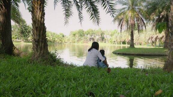 亚洲妈妈和小女孩坐在池塘边休息在公园里与大自然一起享受一家人一起度假享受大自然的生活方式