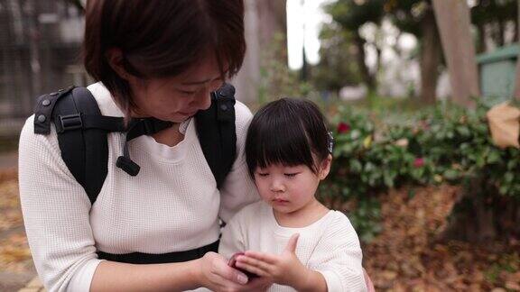哭闹的小女孩和妈妈在公园里玩智能手机