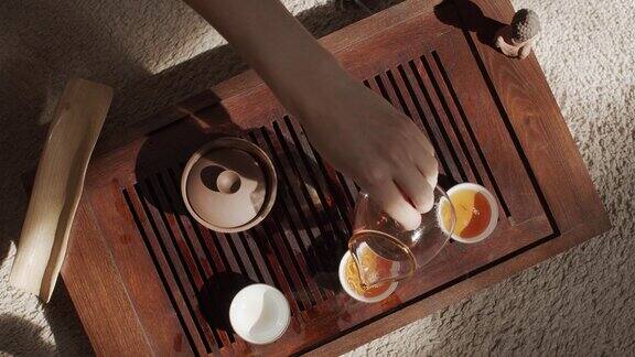 难以辨认的茶大师在小杯子里倒入新鲜的热饮