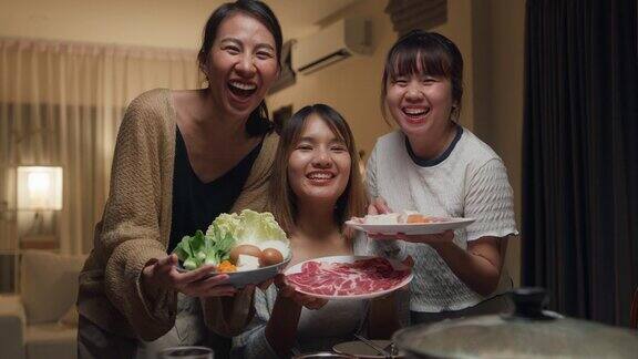 一群快乐的亚洲朋友看着相机自拍视频电话一边吃火锅晚上在家里聚在一起吃春节团圆饭生活方式享受美食