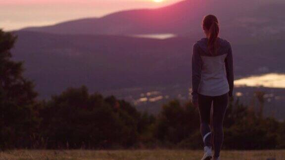 一位年轻女子在日落时分走在山顶上