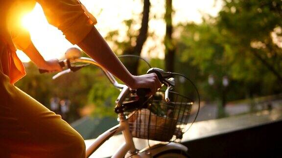 一个不认识的女人的手握把手而骑着一个城市自行车的篮子和鲜花的特写清晨镜头光晕太阳正在上升替身拍摄