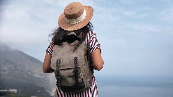 优雅的女游客戴着草帽从山顶欣赏海景