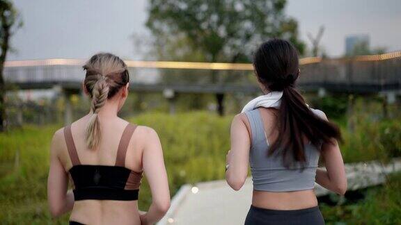 后视镜:两位亚洲美女朋友穿着运动服肌肉完美一起积极慢跑用智能手表监控在公园花园的人行道上积极的生活方式
