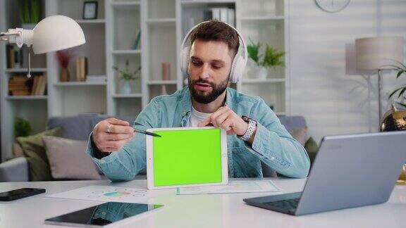 成功的白人男子手持绿屏平板电脑与伴侣在线聊天男性自由职业者在家中与同事进行视频会议时在平板电脑上使用色度键