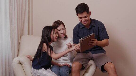 亚洲快乐的父母和漂亮的女儿在客厅里一起使用平板电脑享受家庭时光