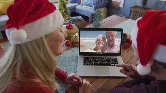 戴着圣诞帽的白人夫妇用笔记本电脑进行圣诞视频通话屏幕上的夫妇