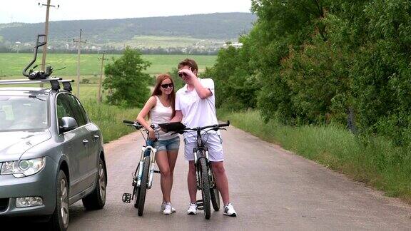 年轻夫妇在自行车附近的汽车与车顶安装自行车承运人