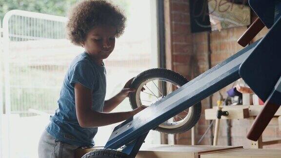 一个十几岁的男孩站在车库的一个工作台前的侧视图和翻转他的赛车背光