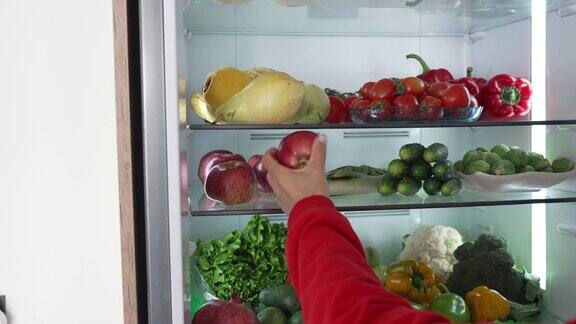 从冰箱里拿生食的女人冰箱里装满了健康食品水果和蔬菜