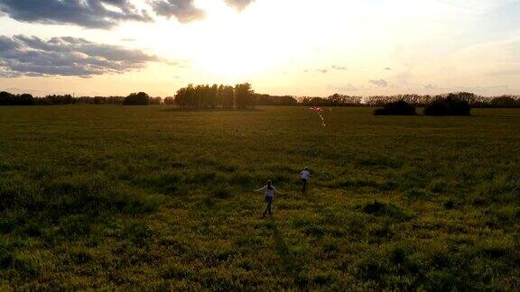 母亲和男孩带着风筝在绿色的田野上奔跑欢声笑语喜庆心情秋天日落