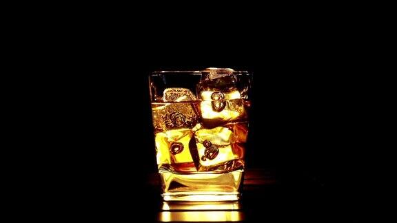 酒保将威士忌倒入装有冰块的玻璃杯中放置在木桌和黑色的背景上重点放在冰块上威士忌放松的时间放在温暖上