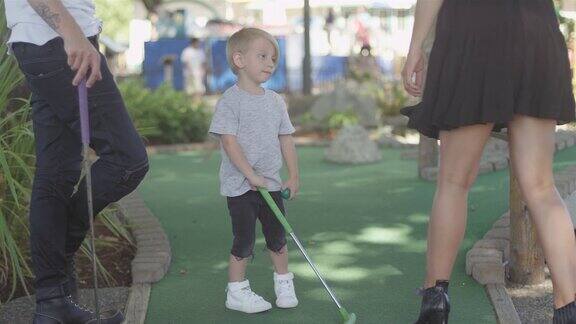 年轻热爱时尚的家庭在公园打高尔夫高尔夫球杆撩起了孩子的衬衫