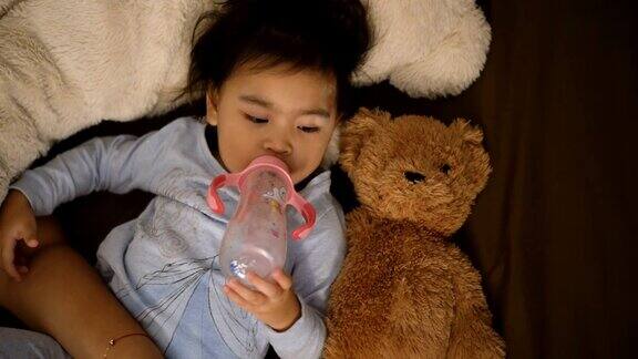一个用奶瓶喝牛奶的亚洲女孩持有的泰迪熊