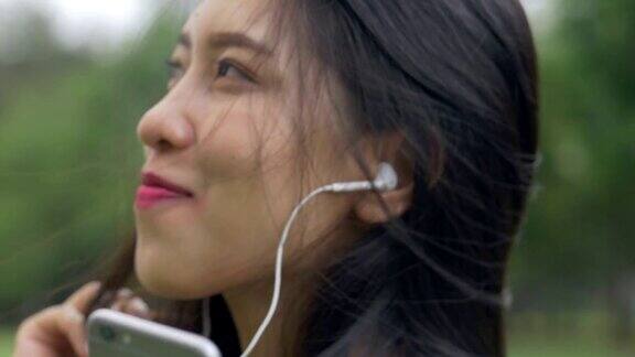 慢镜头美丽的年轻亚洲女子享受听音乐看镜头微笑在公园