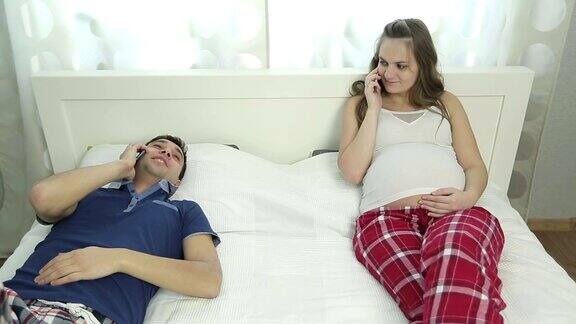 丈夫和他怀孕的妻子躺在卧室的床上用手机聊天