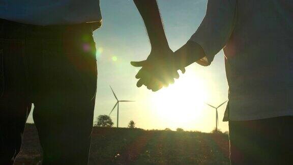落日的剪影两人手牵着手漫步在风力涡轮机之间非常自由援助之手