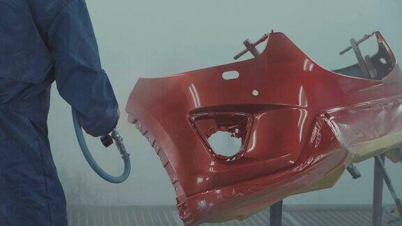 汽车油漆工在专用展台为汽车前保险杠喷涂红漆