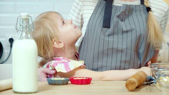 一个可爱的小女孩拥抱妈妈在厨房做饼干或松饼