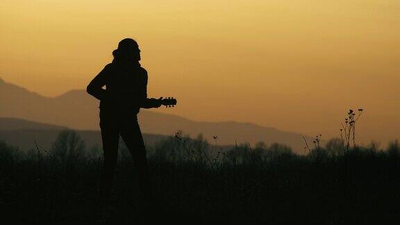日落时分一个年轻女子在大自然中弹吉他剪影