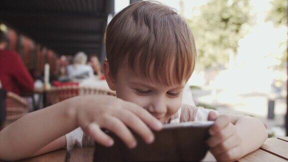 可爱的小男孩在咖啡馆玩智能手机