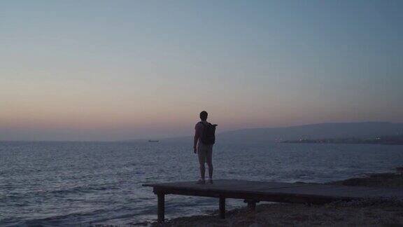 主题是孤独抑郁在旅行中寻找问题的答案一名背着背包的男子在帕福斯市塞浦路斯岛的木制码头上眺望地中海的日落